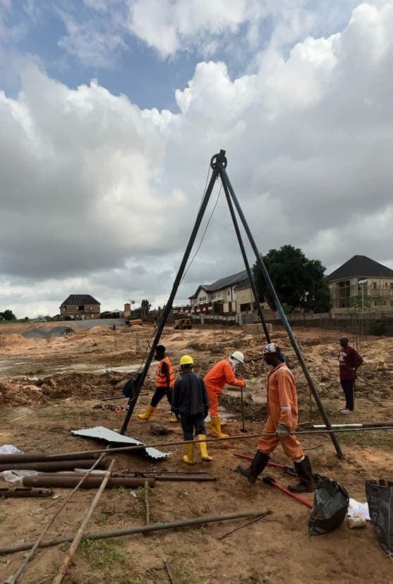The boring rig set up over the trial position, with the crew working the tripod and winch on the cleared site
